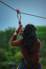 Woman zip-lining in India,  back view, lush green backdrop.
