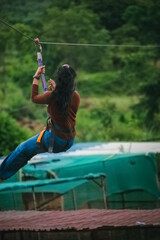 Young woman ziplining through lush green landscape in India. Dynamic action shot.