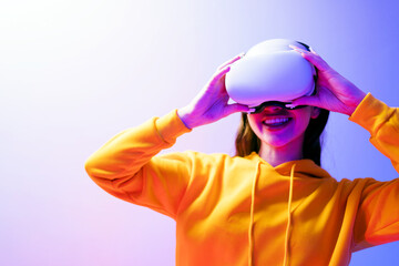 Smiling young woman in orange hoodie adjusts VR headset in colorful studio. Concept of virtual...