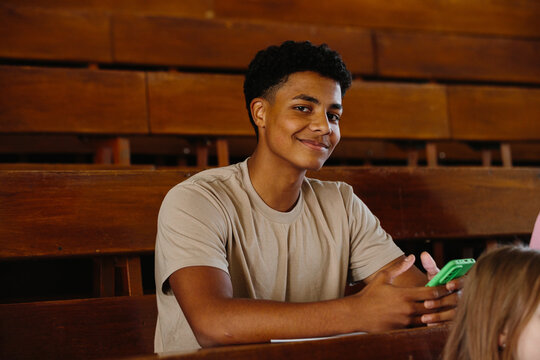Smiling Young Man with Mobile Phone in a Wooden Auditorium