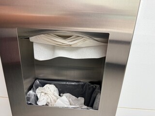 Paper towel dispenser in public restroom with trash below, hygiene and hand drying station, clean...