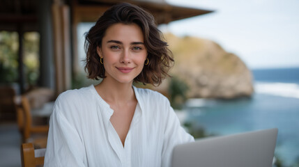 young business woman sitting with laptop at a wooden table in an open-air cafe built on a rocky cliff above the sea, early morning sunrise light, ocean view in background, casual o