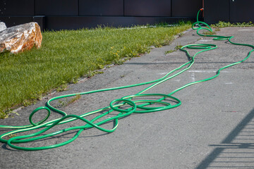 A watering hose lies on the sidewalk on a summer day
