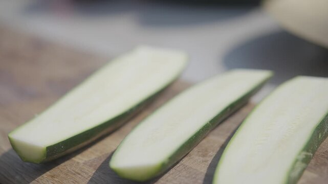 Three pieces of zucchini are cut into slices on a cutting board. The slices are arranged in a row, with one slice slightly overlapping the other two. Concept of preparation for a meal