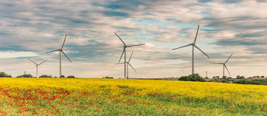 Wind turbines stand tall in a field of yellow flowers, generating clean energy against a backdrop of a cloudy sky