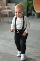 cute little boy with blue eyes and suspenders smiling and looking away on a blurred background