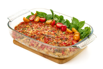 Oven-baked tomato and vegetable casserole in glass dish, isolated on white background.