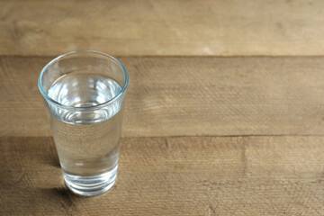 water glass on wooden table, closeup. Drinking clear water in the morning for health. Space for text 