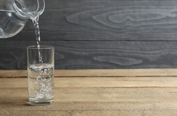 Pouring water from jug into glass at wooden table, closeup. Drinking clear water in the morning for...