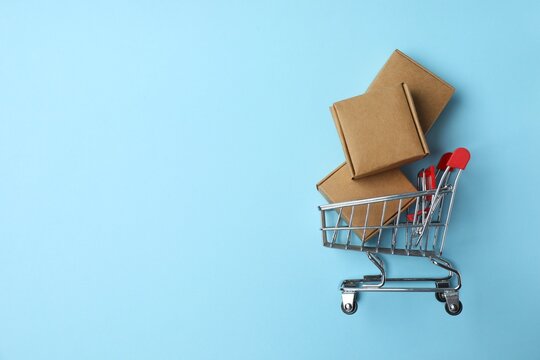 Shopping concept. Close up photo of small shopping cart with cardboard box on blue background with copy space
