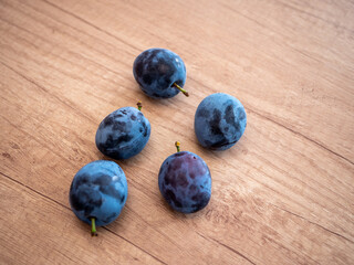 Five fresh blue plums on wooden surface. Natural and ripe fruit perfect for food, diet, harvest, healthy eating and seasonal themes.