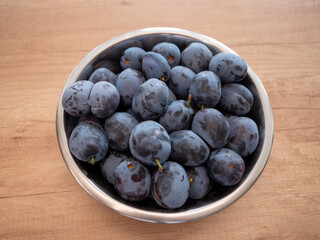 Metal bowl filled with ripe Prunus domestica plums on wooden surface. Natural source of fiber, antioxidants and vitamins, supports digestion and immune system.
