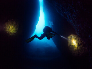 diver with flashlight diving between the rocks of an underwater cave, concept of scuba diving and...