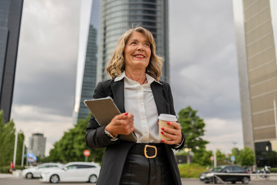 Businesswoman with coffee and tablet in urban cityscape outdoors