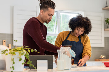 African American couple stirring ingredients in ceramic mixing bowl on kitchen island with tablet