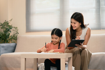 Asian mother using a digital tablet while helping her daughter with homework at home