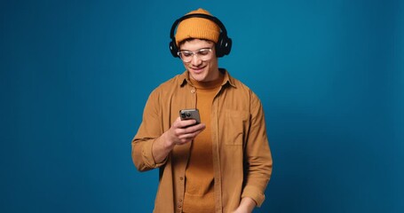 Man, headphones and smile with phone in studio, streaming and music subscription on blue background. Person, smartphone and listen with mock up space, mobile app and happy for album release on web