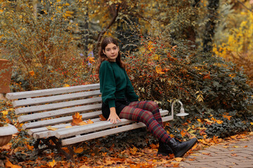 Teenage girl 13 years old in green sweater sitting on bench in autumn park. autumn season. autumn concept. fall