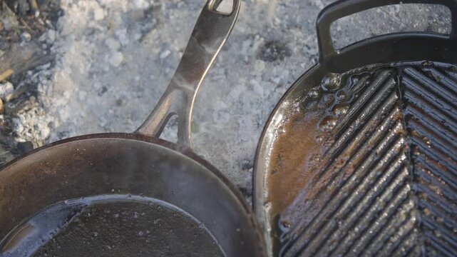 A pan with smoke coming out of it is next to a pan with burnt food on it. Scene is somewhat sad and disappointing, as the food appears to be overcooked and burnt