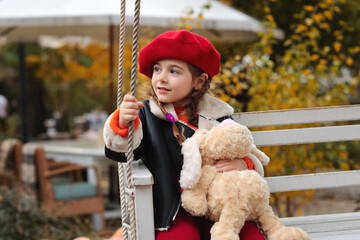 Happy beautiful baby girl in red beret in autumn park riding on swing. autumn concept. autumn mood. fall