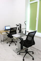Modern ophthalmologist office interior with slit lamp biomicroscope, desk with laptop, and two...