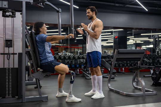 Asian woman with prosthetic leg from amputation from doing weight training workout exercise using machine at gym with professional trainer for handicap and disability people and recovery concept - Powered by Adobe