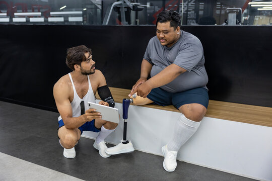 Gym trainer giving advice to people with disability to do walking workout exercise at gym by looking at the plan from digital tablet for healthy and recovery concept