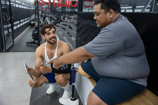 Gym trainer giving advice to people with disability to do walking workout exercise at gym by looking at the plan from digital tablet for healthy and recovery concept