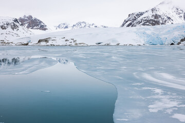 Floating ice on the ocean with blue glacier and mountains in the background in the arctic of Svalbard, Norway © Reto Ammann