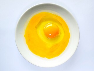 Fresh raw egg yolk in ceramic plate isolated on white background. Raw egg yolk. Cracked egg in a white bowl, ideal for culinary and kitchen themes. Top view.