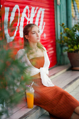 A beautiful teenage model girl posing on the streets of old town during street style photo shooting drinking ice fruit beverage