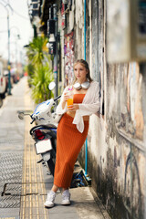 A beautiful teenage model girl posing on the streets of old town during street style photo shooting drinking ice fruit beverage