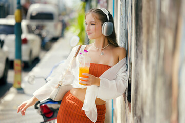 A beautiful teenage model girl posing on the streets of old town during street style photo shooting drinking ice fruit beverage
