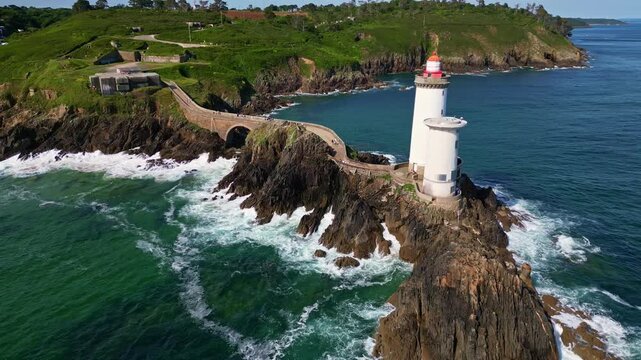 Aerial shot retreating from the Petit Minou lighthouse in Brittany, showing the stone path, arch bridge, rocky cliffs and crashing waves - France