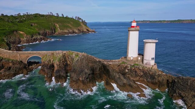 Orbital drone shot from left to right around Petit Minou lighthouse, showing the side path, crashing waves, and rocky cliffs. Brittany in France