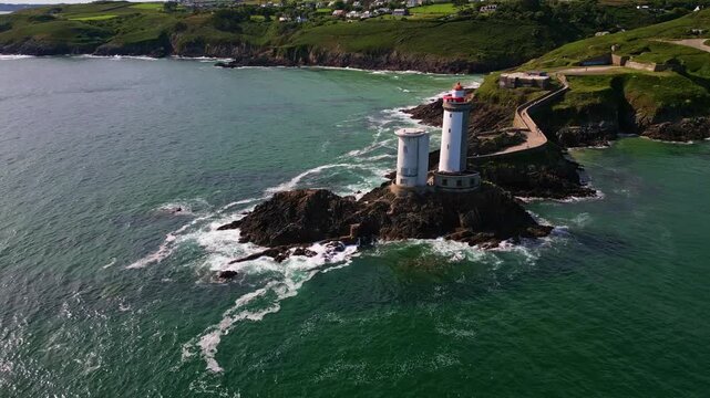 Drone performs a lateral movement above the sea, revealing the Petit Minou lighthouse, stone path, crashing waves, cliffs and surrounding vegetation - Brittany in France