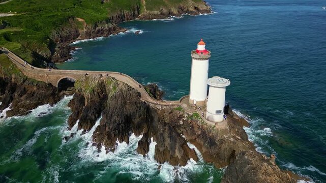 Drone lateral shot revealing the Petit Minou lighthouse from the stone path, with green cliffs in the background and the ocean below. Plouzan&eacute;. Brittany in France