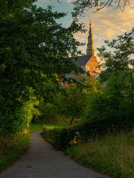 Spiral tower of the Church of Our Savior rises above lush trees, seen from Christianshavns Vold on a sunny day in Christianshavn, Copenhagen, Denmark