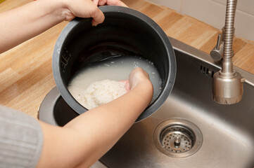 Person rinsing white rice in a pot under sink water, preparing rice for cooking by removing excess starch in kitchen setting