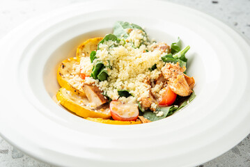 Fresh salad with grilled chicken, couscous, cherry tomatoes, spinach, and roasted squash in a white...