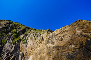 Steep rocky cliff with patches of green moss under a clear bright blue sky.