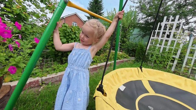 A little child girl in a dress swings on a big round swing in summer. Shot on an action camera. amara, Russia - 10 July 2025