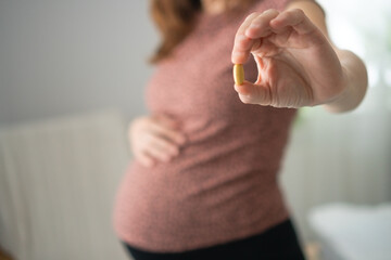 Pregnant female carefully examining pill before intake while touching her bump. Thoughtful health...
