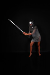 Slender female knight in chainmail and helmet holding sword full length low key portrait