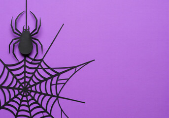 A Paper Cutout of a Black Spider Hanging from a Web on a Solid Purple Background, with Ample Horizontal Copy Space, Perfect for Spooky Halloween Designs