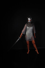 Slender female knight in chainmail and helmet holding sword full length low key portrait