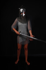 Slender female knight in chainmail and helmet holding sword full length low key portrait