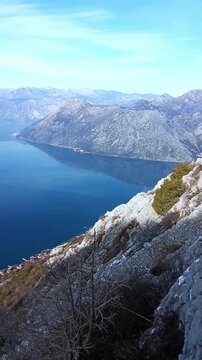 Panoramic hiking view above Dobrota, Montenegro: old stone trail along the mountainside and a breathtaking vista of the Bay of Kotor with Adriatic sea waters, majestic peaks and tiny coastal towns