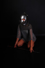 Female knight in chainmail and helmet sitting on her knees and holding sword low key portrait