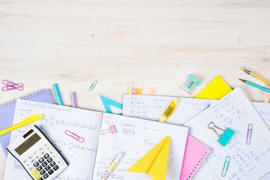 Exercise book white sheets with formulas, multicolor office supplies and calculator on wooden table background with space for text